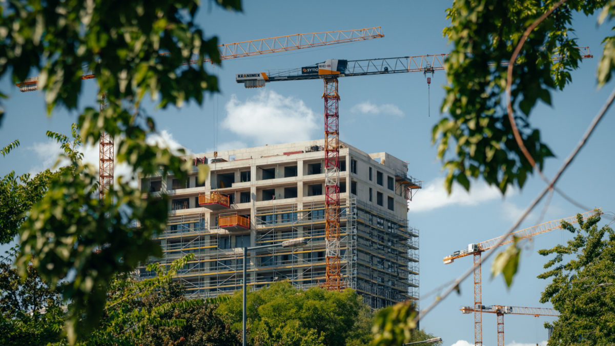 Im Bau befindliches Hochhaus mit Kränen, durch üppig grüne Bäume gesehen.
