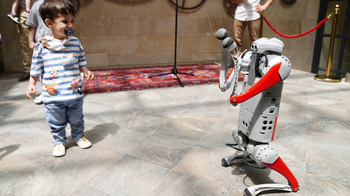 Ein kleiner Junge interagiert mit einem humanoiden Roboter während einer Indoor-Technik-Ausstellung, was zukünftige Innovation symbolisiert.