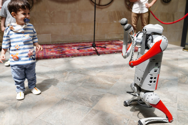 Ein kleiner Junge interagiert mit einem humanoiden Roboter während einer Indoor-Technik-Ausstellung, was zukünftige Innovation symbolisiert.